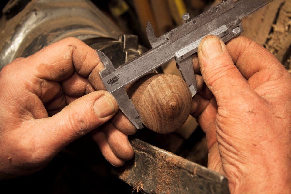 Close-up of a craftsperson's hands measuring a wooden piece with calipers