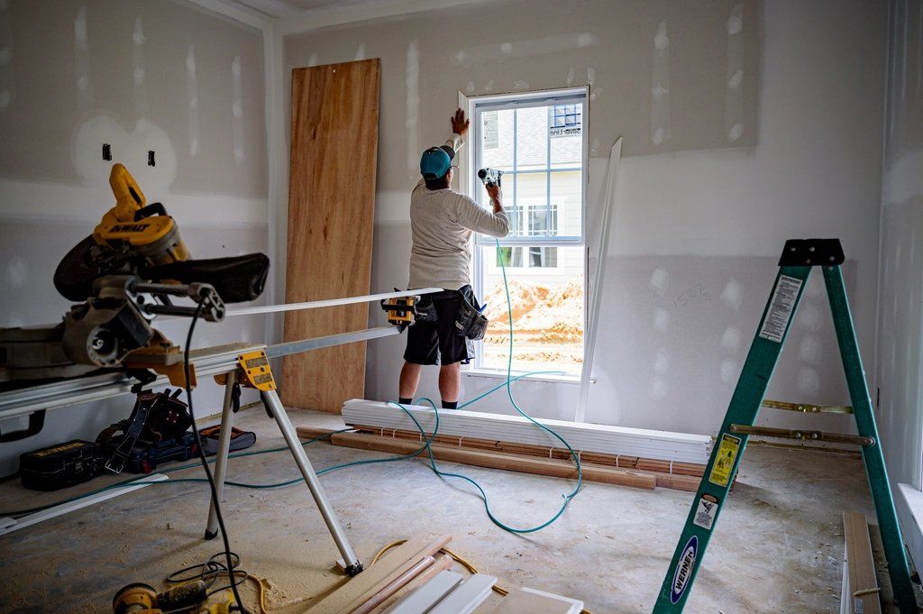 Room with new drywall, a worker fitting a window, a stepladder and a mitre saw set up on site