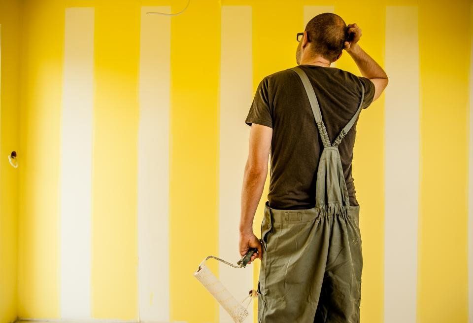 Person seen from behind holding a paint roller in front of a freshly painted yellow striped wall