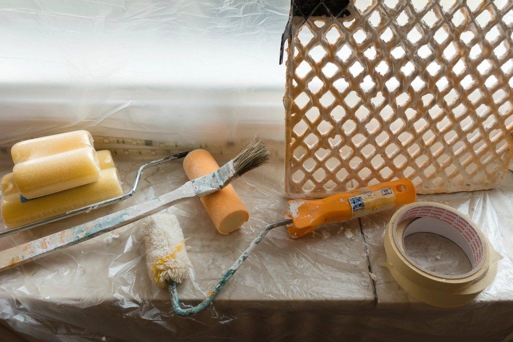 Painting and finishing supplies: putty knife, brushes, sponge and masking tape on plastic sheeting