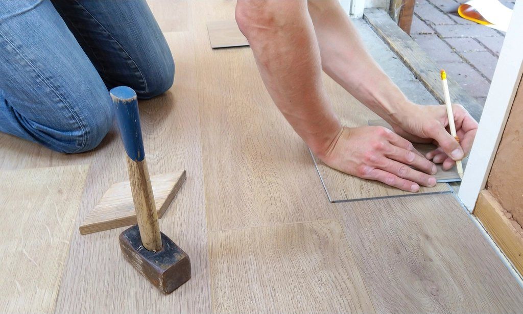Hands marking a plank during floor installation, with a mallet beside