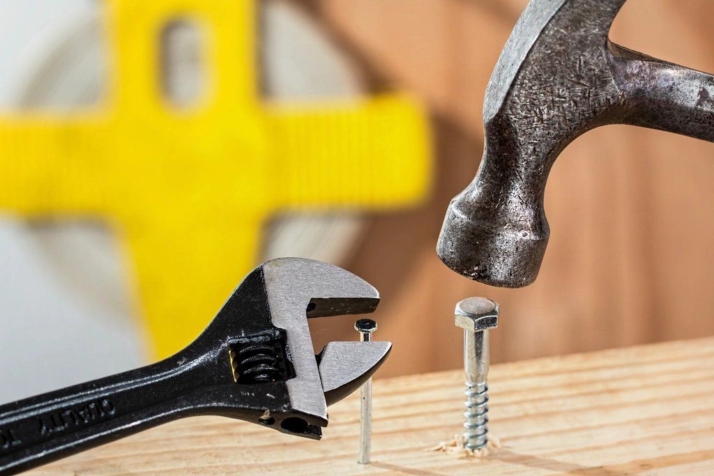 Hammer and adjustable wrench working on a screw and nail in a wood board